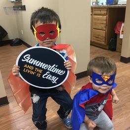 Picture of two young boys wearing super hero capes and masks in a dental office waiting room.